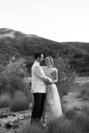 A couple in wedding attire embraces in a scenic mountain landscape at sunset.