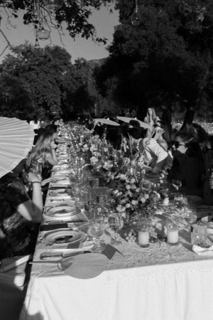Black and white photo of elegant table setting with parasols and floral arrangements.
