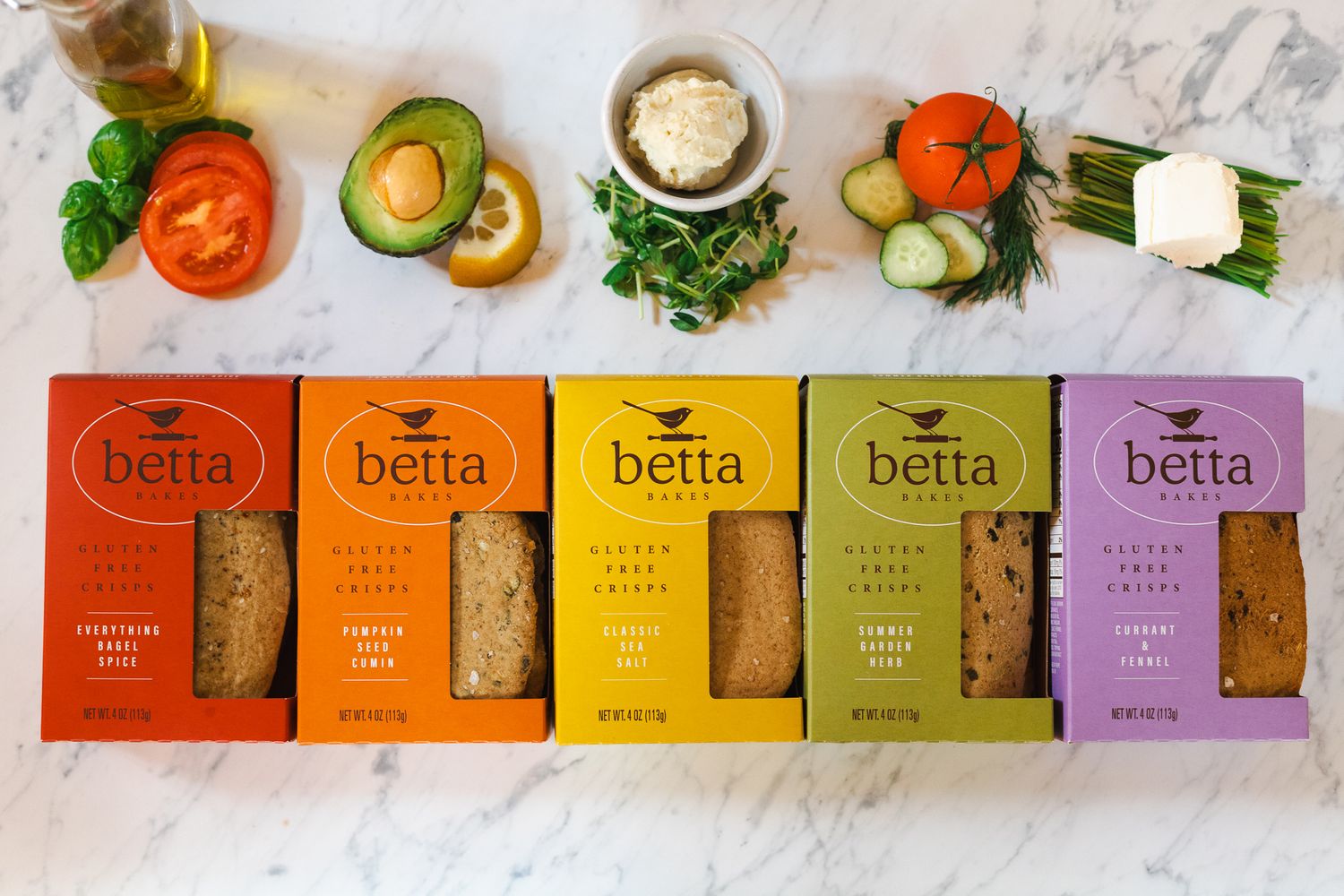 Top down image of 5 gluten free cracker boxes in raibbow colors and flavors for Betta Bakes paired with cracker topping suggestions.