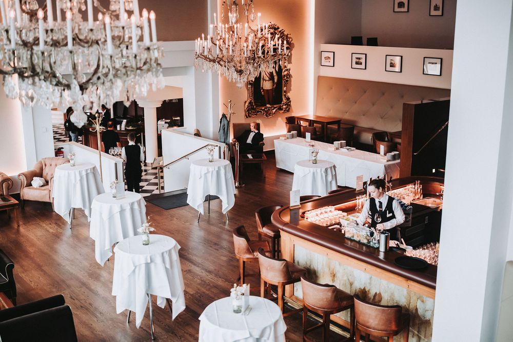 Elegant wedding reception venue with crystal chandeliers and white table settings in a warm-lit room.