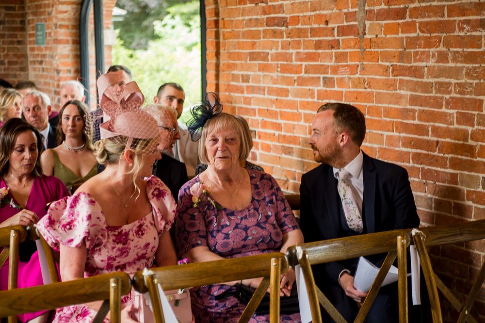 Wedding guests seated in rows watch ceremony proceedings in a brick-walled venue.