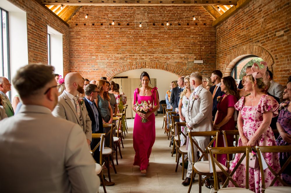 Wedding ceremony in progress with guests seated in a long brick-walled room with vaulted ceiling.