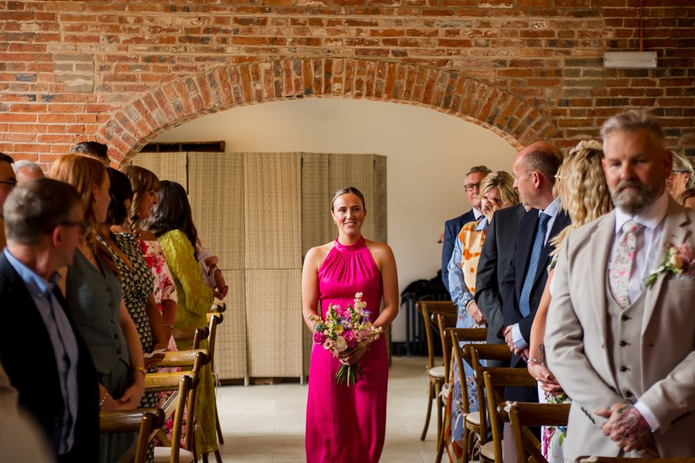 Wedding guests celebrate during a ceremony in a rustic brick-walled venue with string lights overhead.