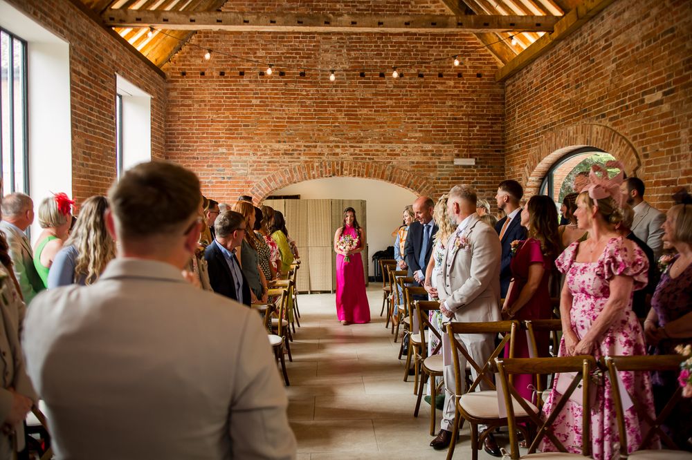 Interior of a rustic brick barn venue decorated with string lights and filled with wedding attendees.