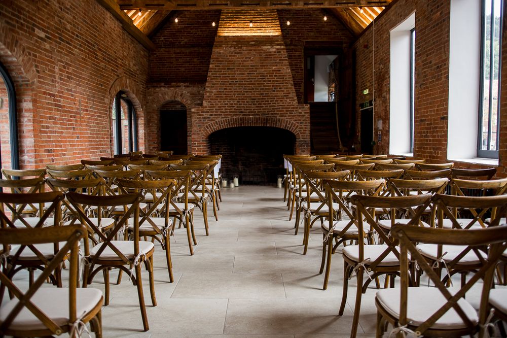 Empty wooden cross-back chairs arranged in rows inside a rustic brick venue with vaulted ceilings.