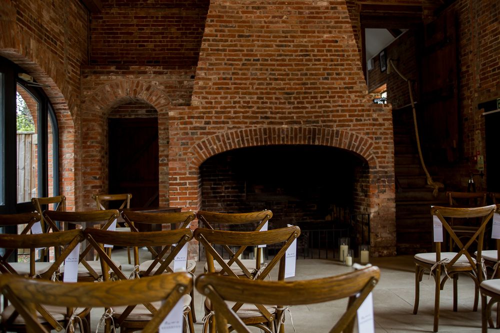 Interior view of an empty wedding venue with exposed brick walls and wooden cross-back chairs.