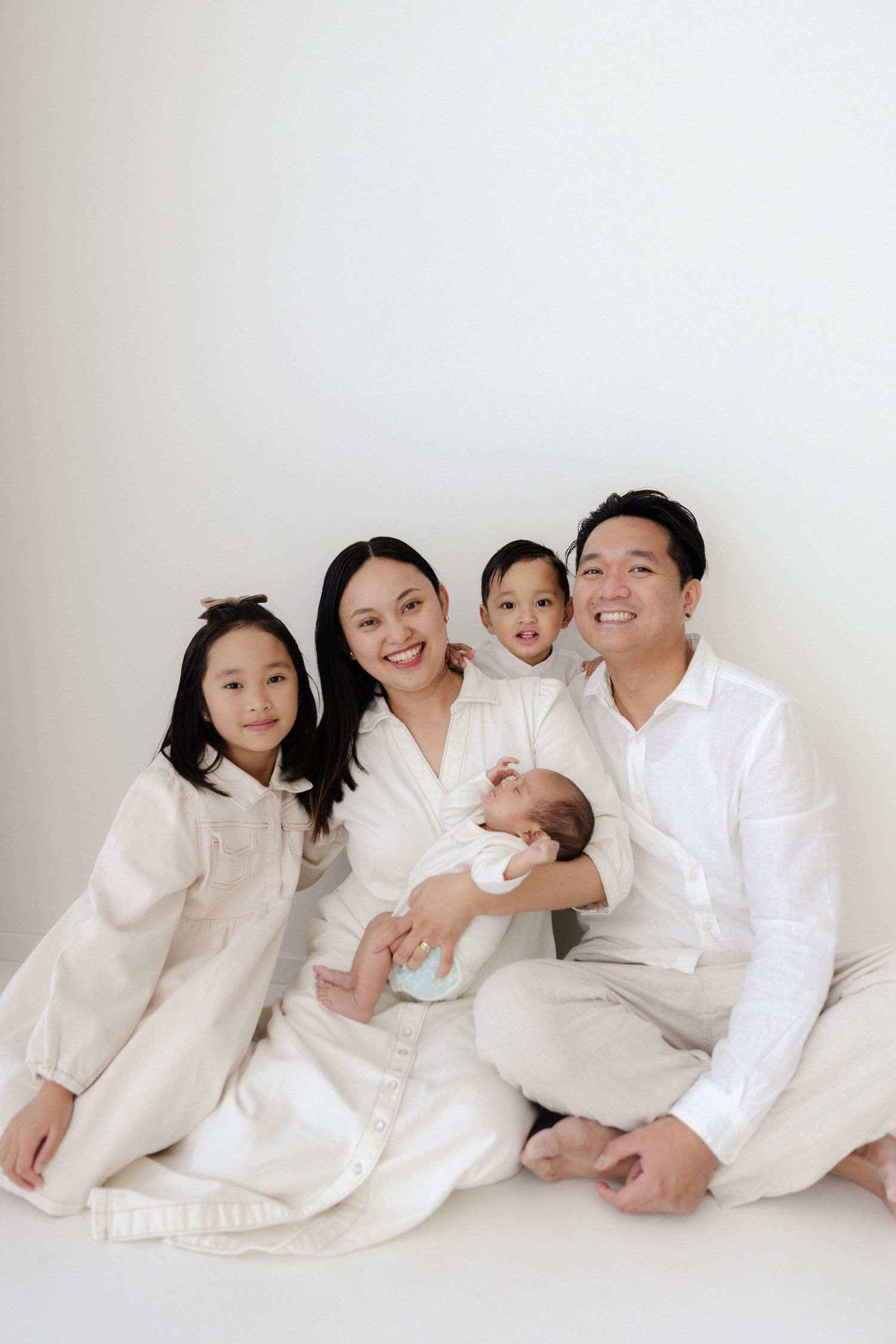 Family portrait in all white clothing against white background showing playful interactions.