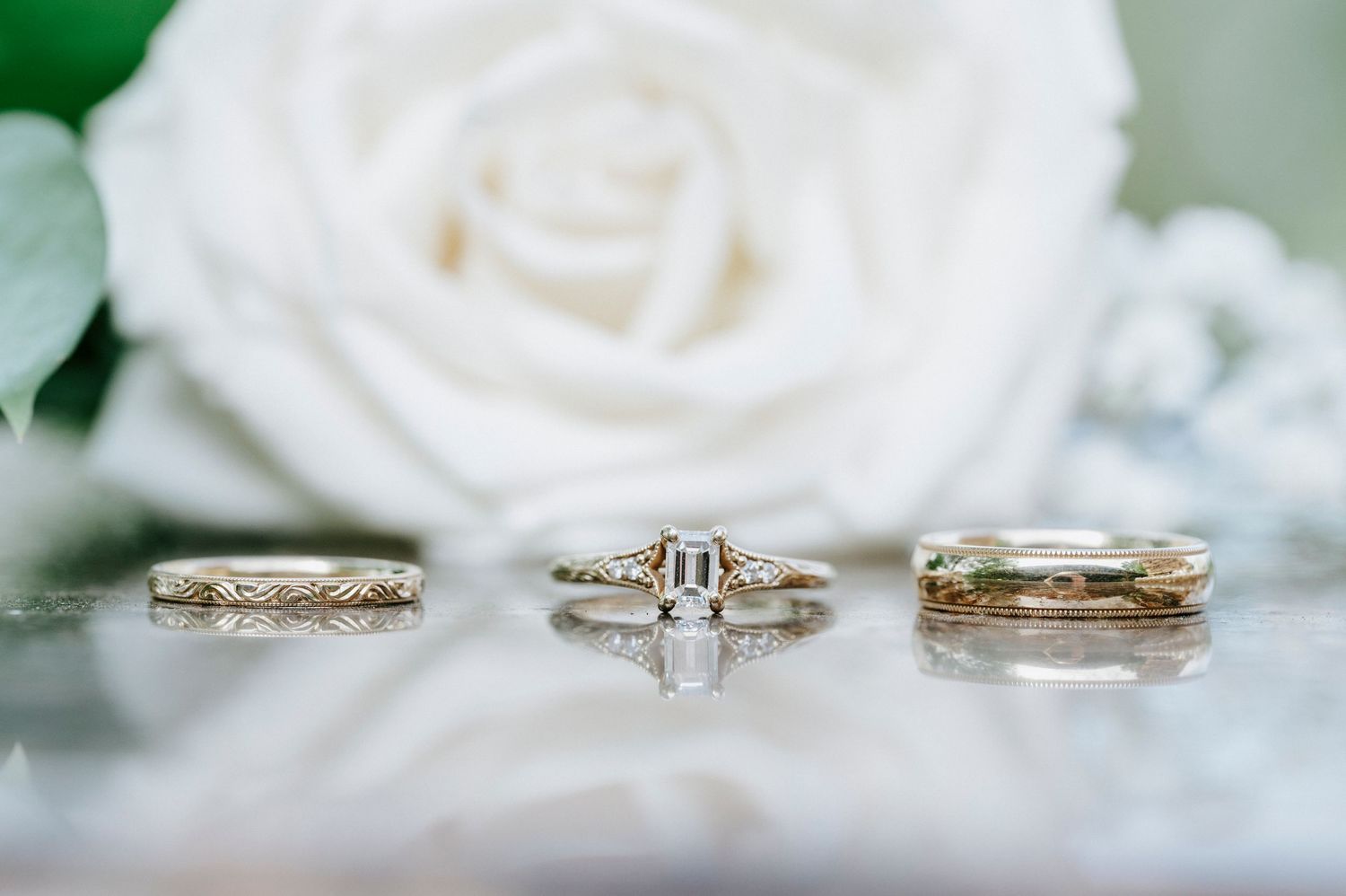 Three elegant diamond wedding rings arranged on a white rose petal with soft focus background.