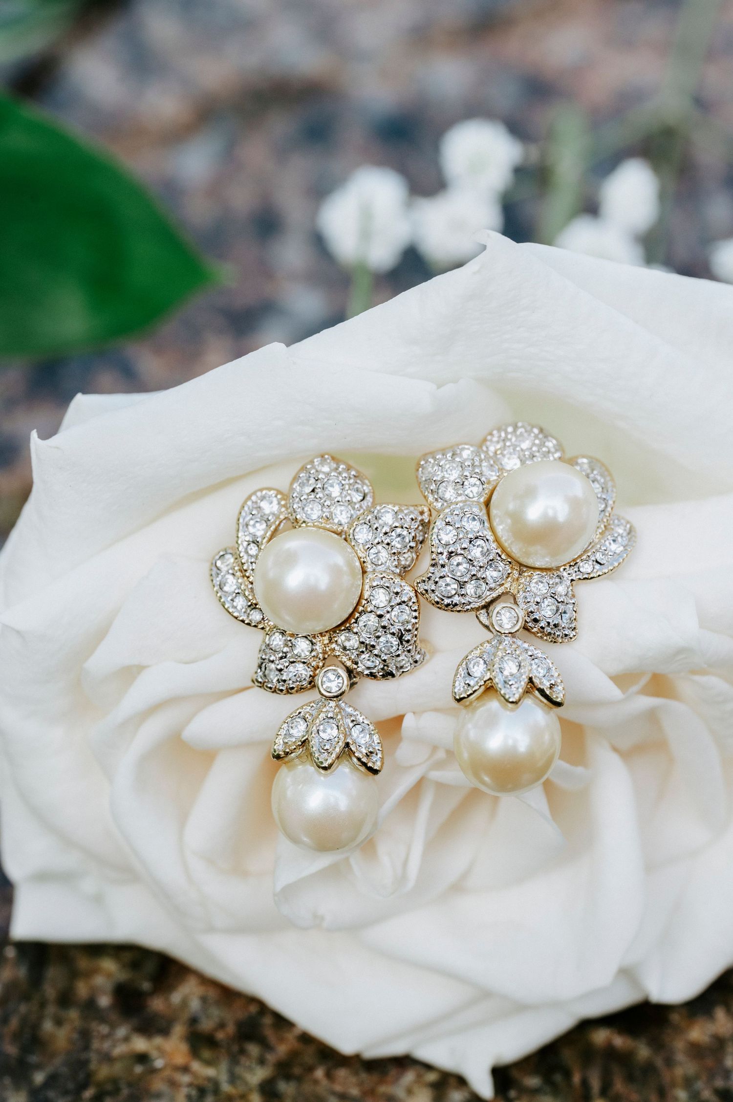 Pearl and crystal floral stud earrings displayed on delicate white rose petals against a natural background.