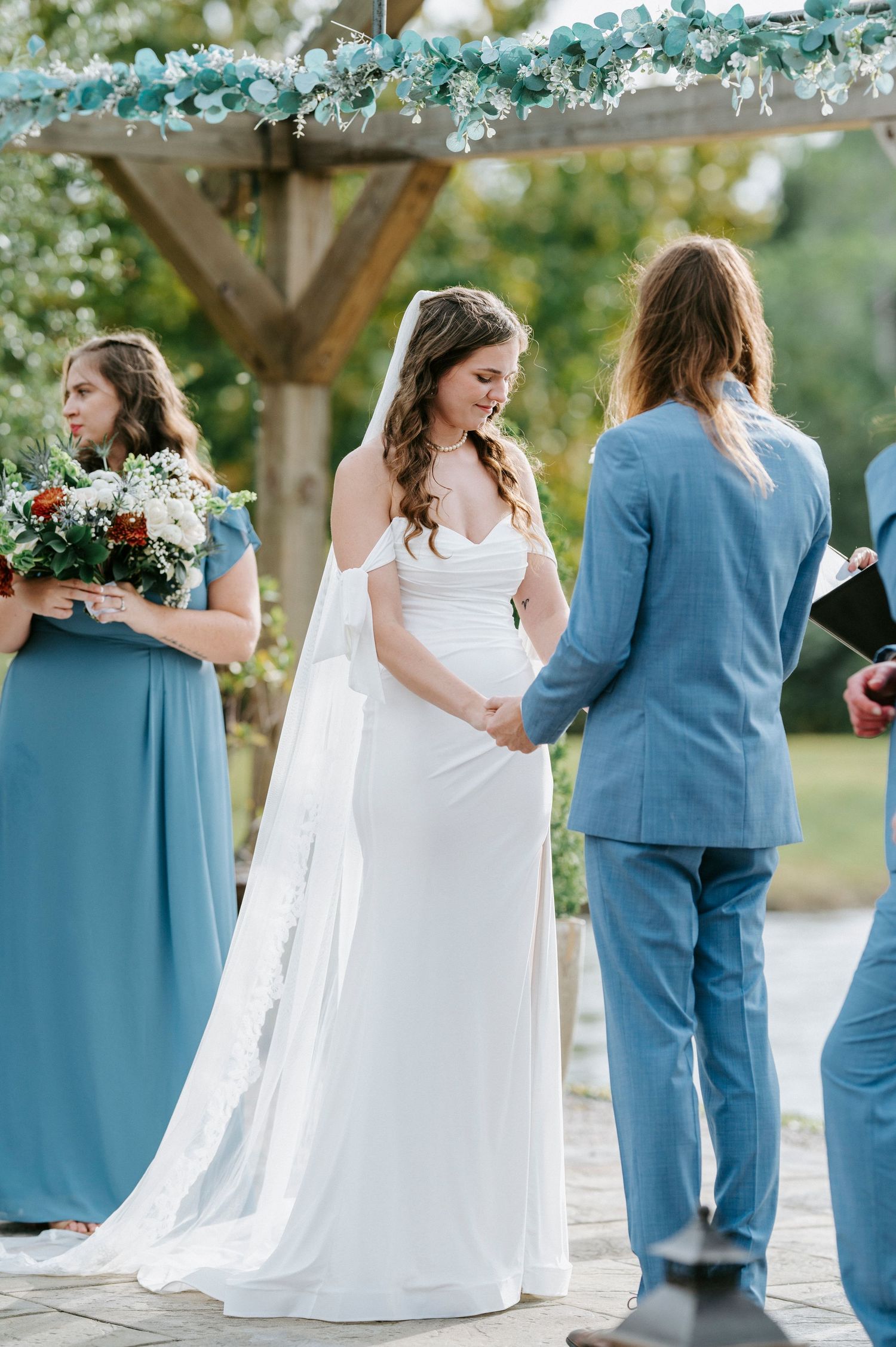 Wedding couple in white dress and blue suit share intimate moments during outdoor photo session under floral decor.