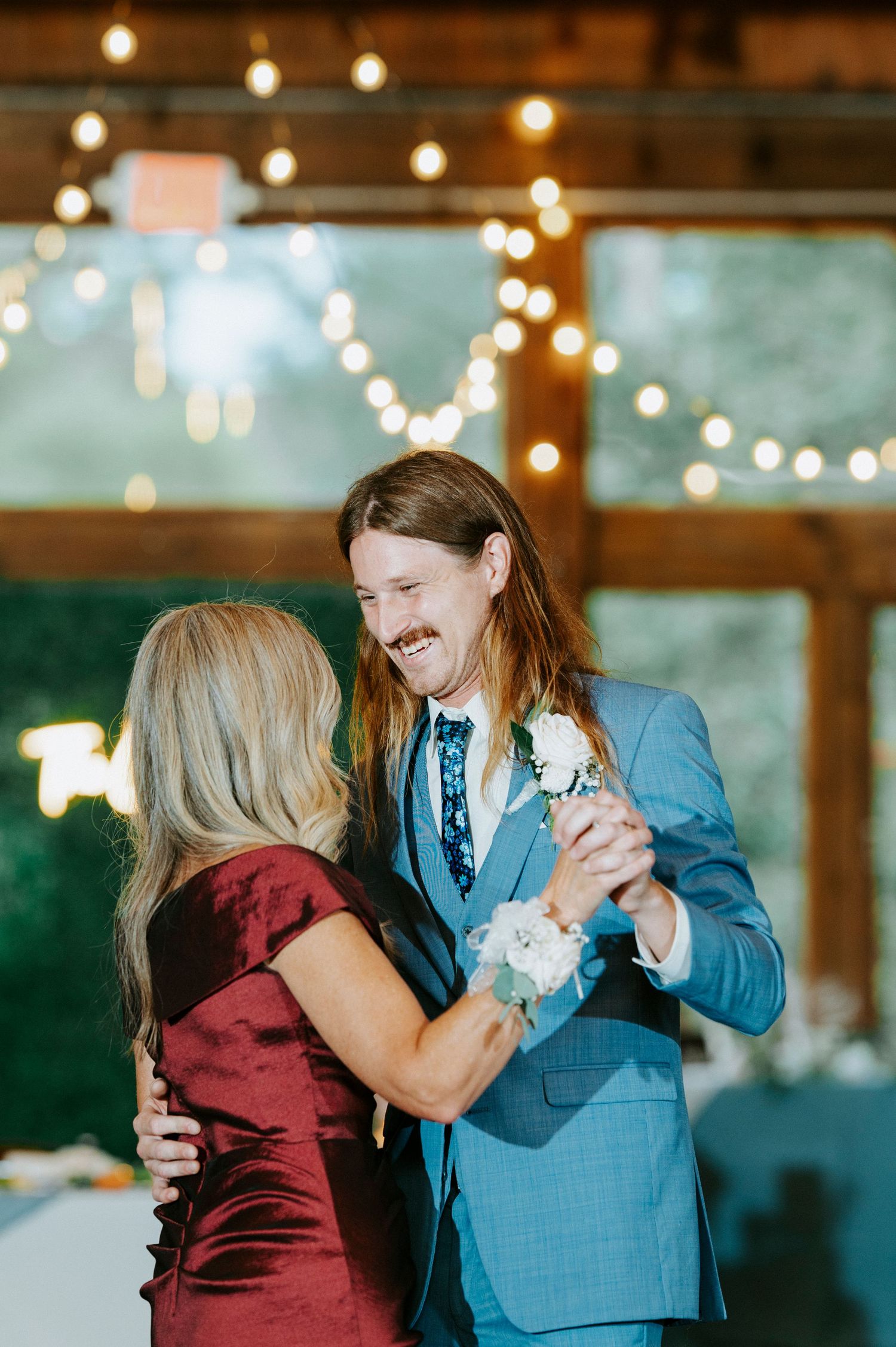 A couple dancing together at a wedding reception with string lights glowing warmly in the background.