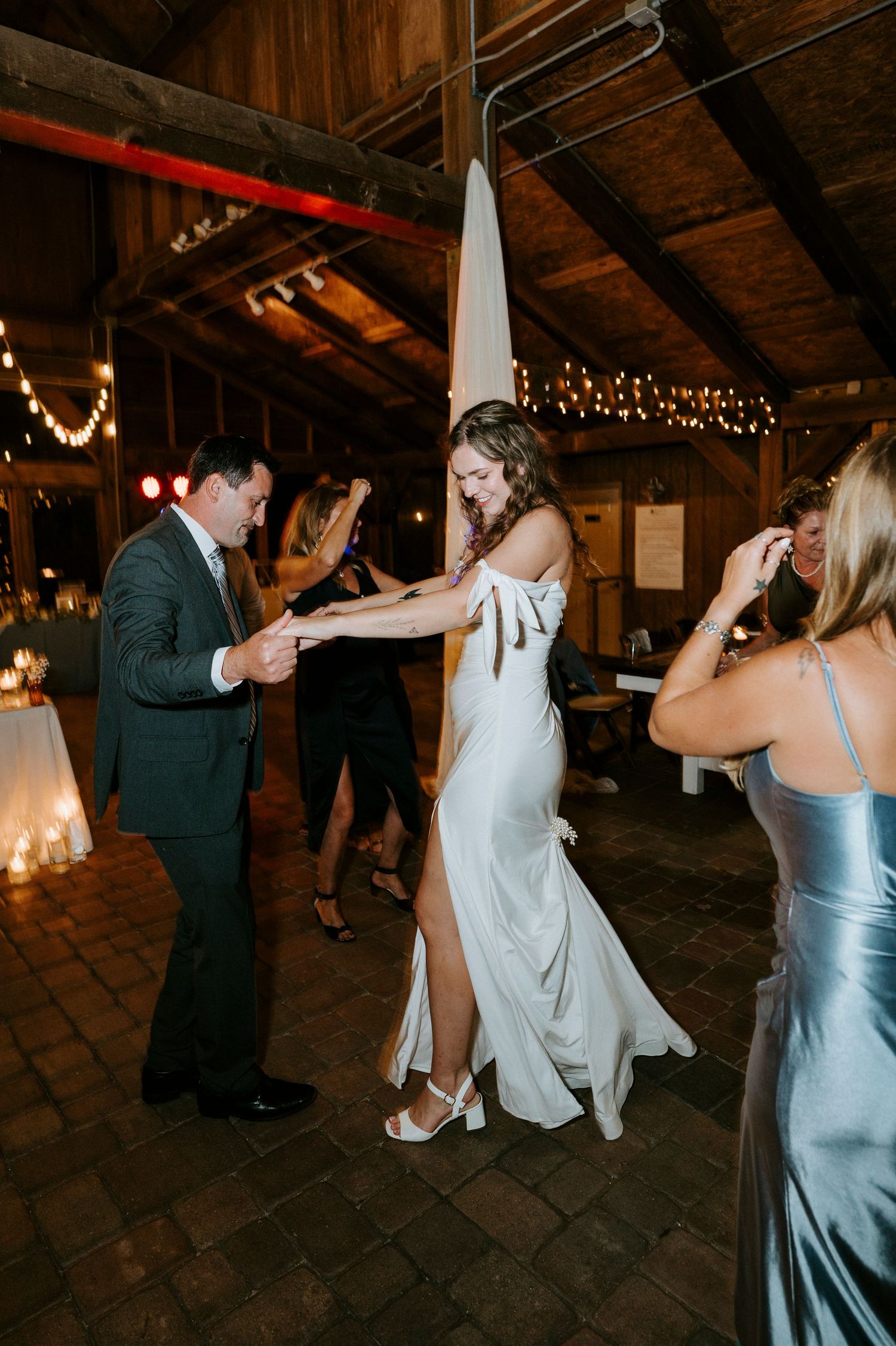 Wedding guests dancing and twirling on a rustic wooden dance floor illuminated by overhead string lights.