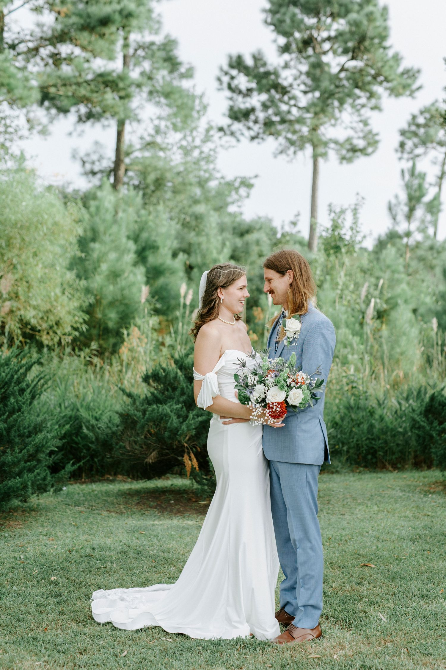 A romantic wedding couple shares intimate moments in a pine forest setting wearing blue suit and white gown.