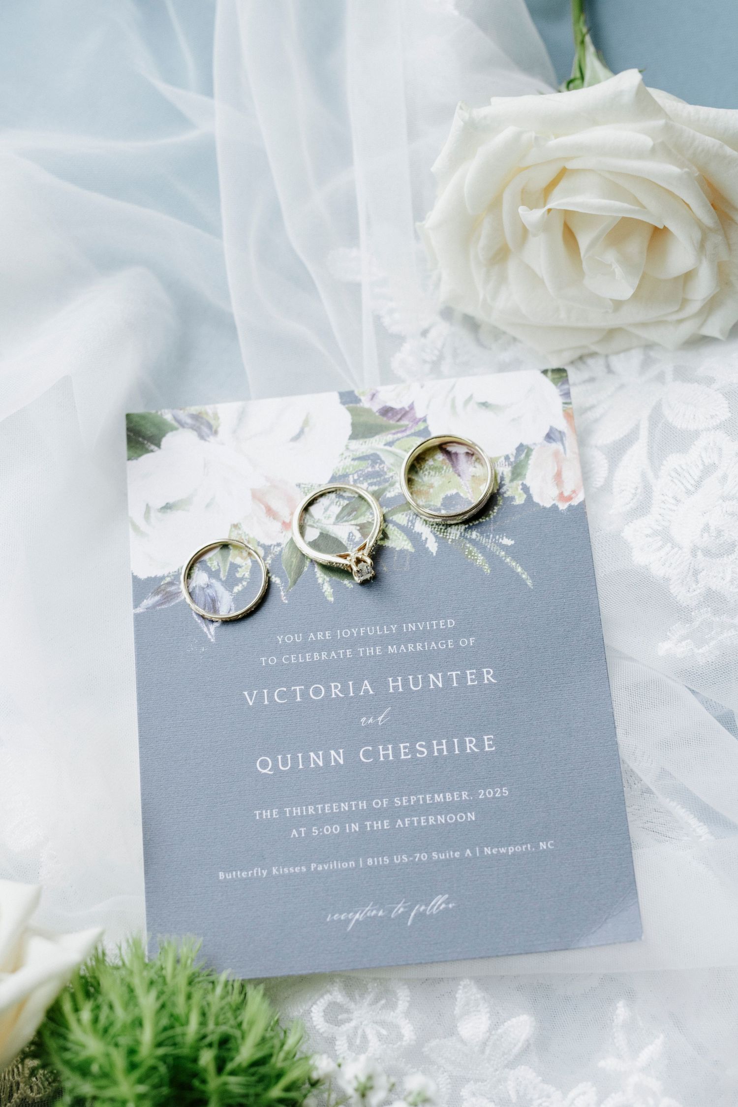 Elegant gray wedding invitations with white roses and engagement rings on a light background.