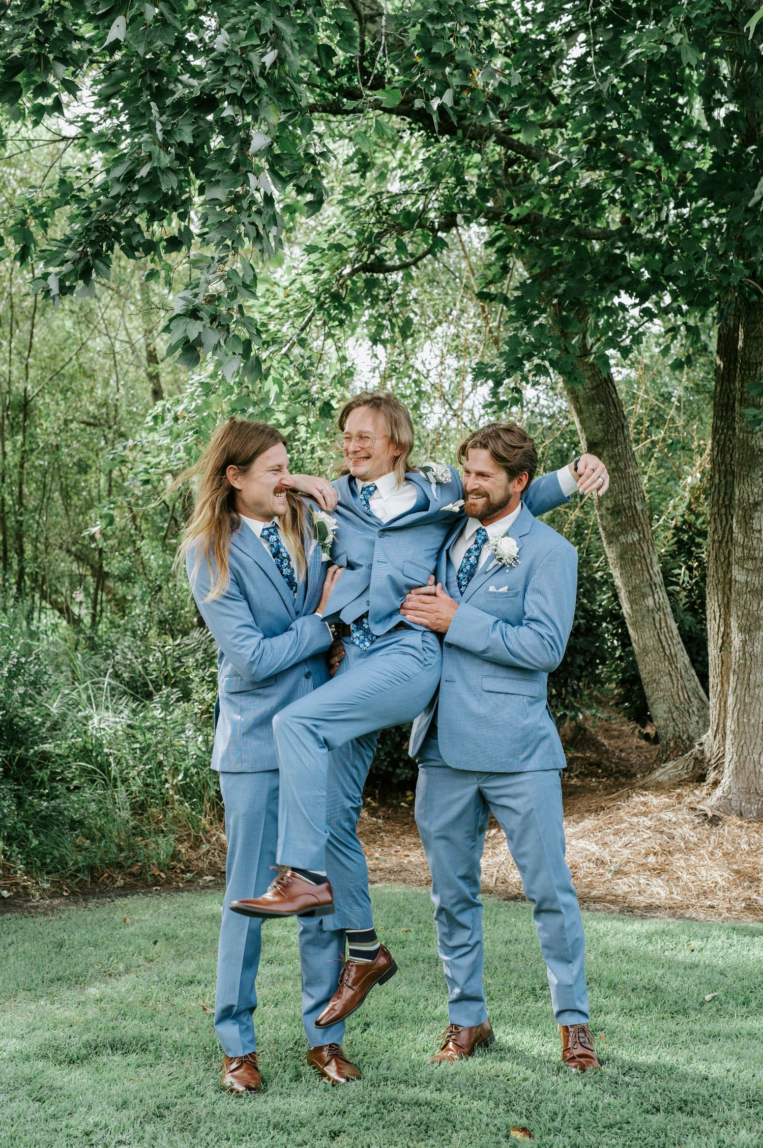 Groomsmen in matching blue suits strike playful poses and share laughs during outdoor wedding photos.