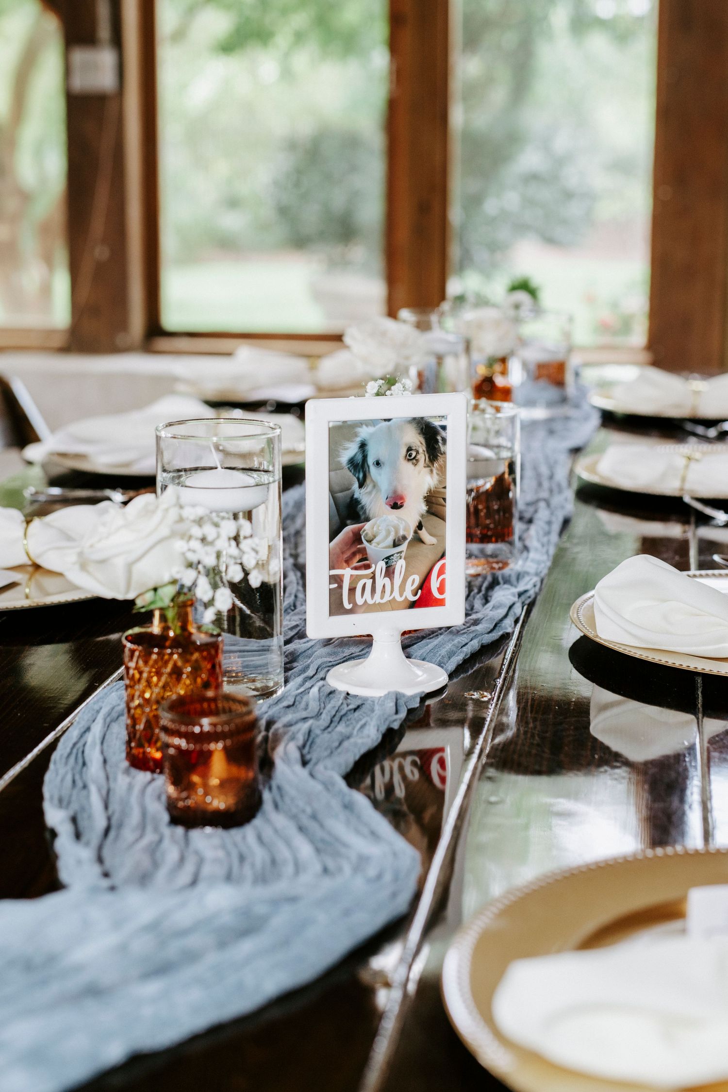 Wedding reception table setting with blue table runner, glass centerpieces and elegant place settings.