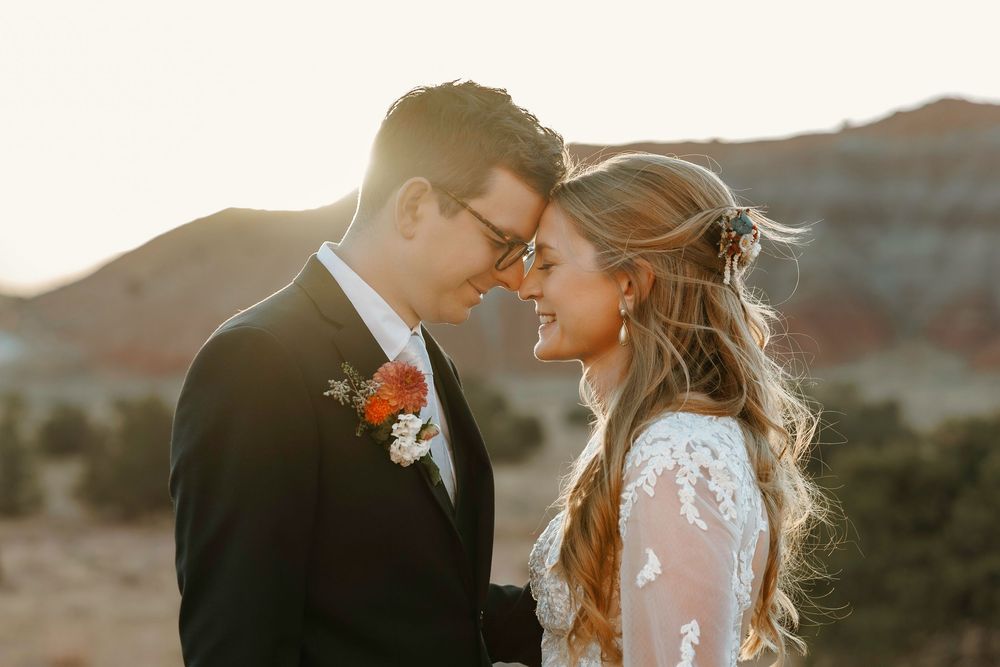 New Mexico newlyweds share an intimate moment at sunset, groom in black tux with orange boutonniere in desert setting.