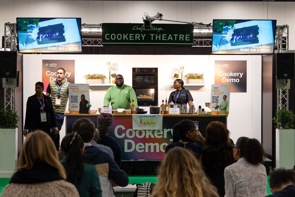 A crowd gathers to watch a cooking demonstration in front of a cookery theatre with digital displays at the 2025 WTM event in London.