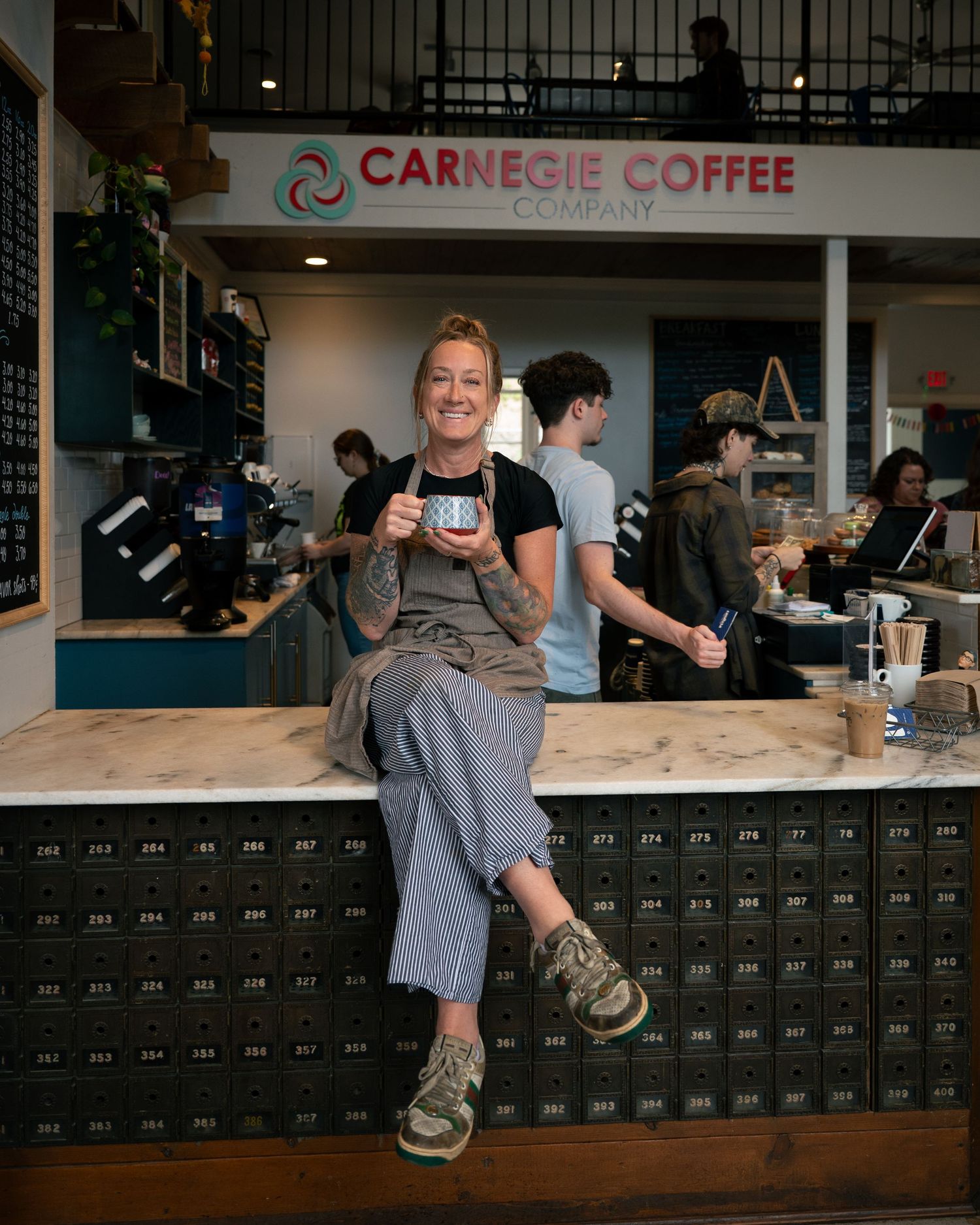 Customers gather at a coffee shop counter with Carnegie Coffee signage visible in the background.