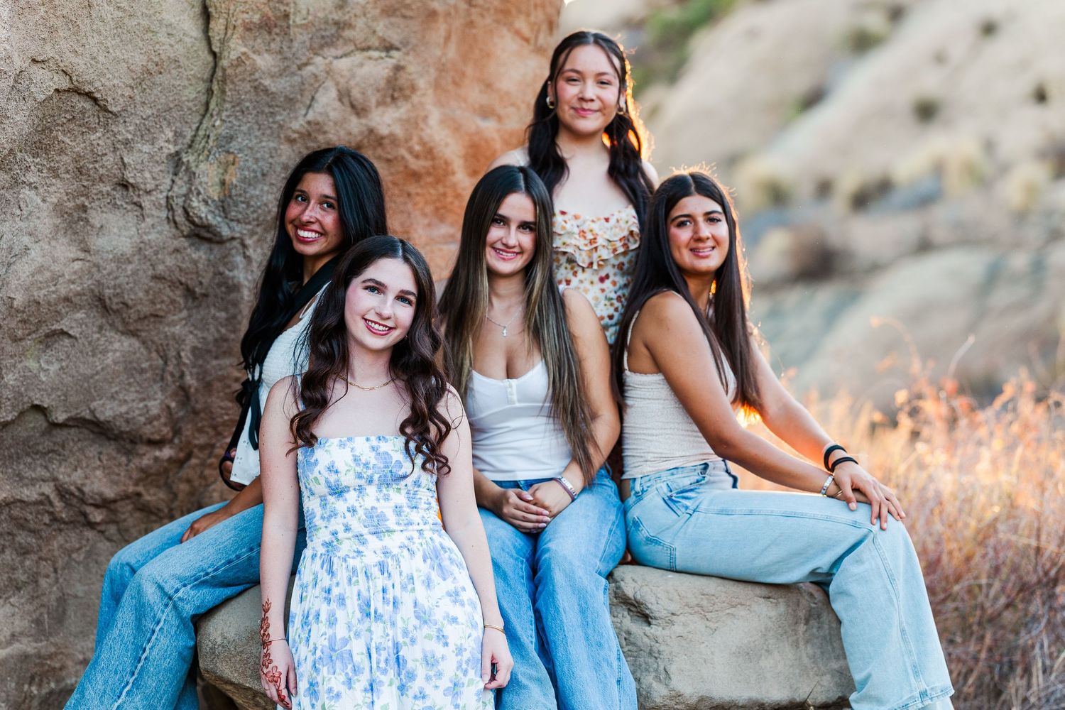 A group of friends in blue and white outfits pose together on rocky terrain during golden hour.