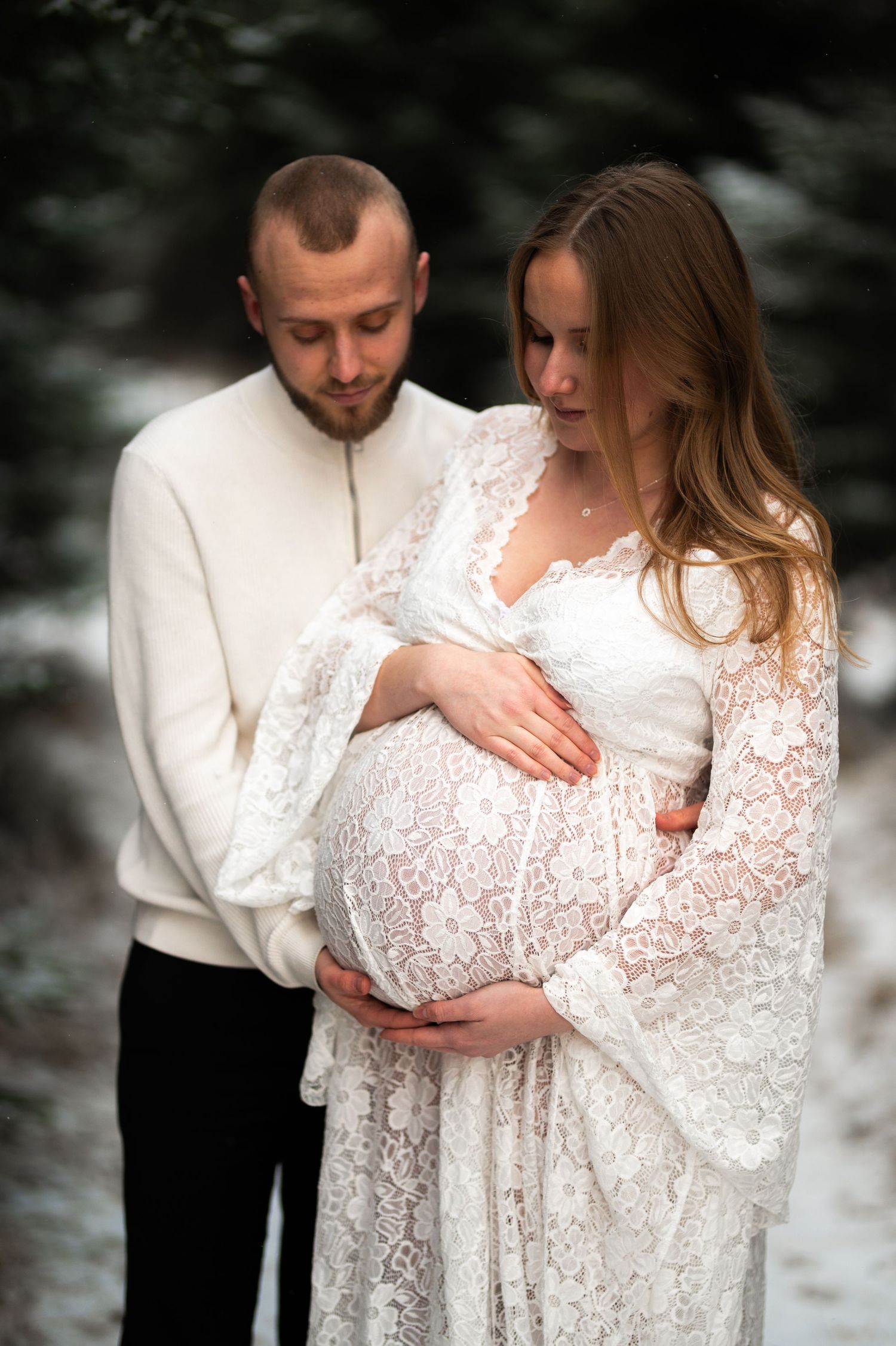 Par som står och tittar ner på kvinnans gravida mage med längtan efter det nya tillskottet