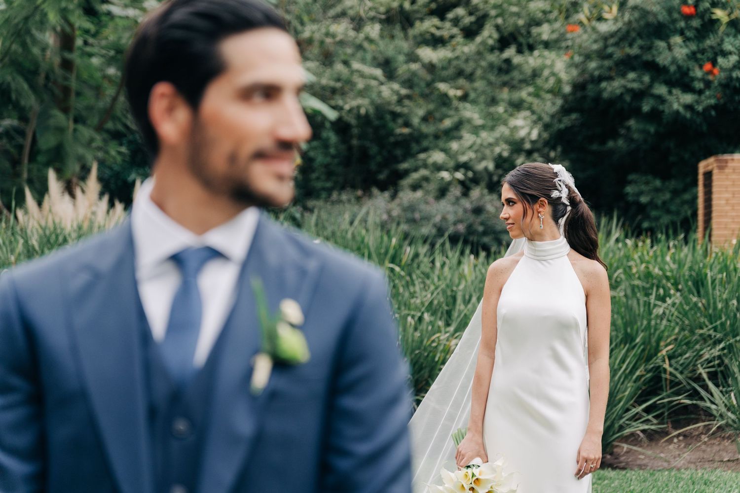 A couple in wedding attire stands together in a lush garden setting during their outdoor ceremony.
