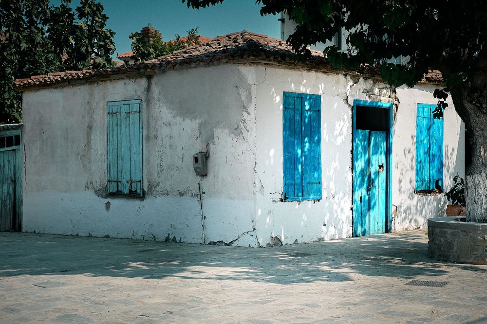 A series of white buildings with bright turquoise blue doors and windows along a Mediterranean-style street.