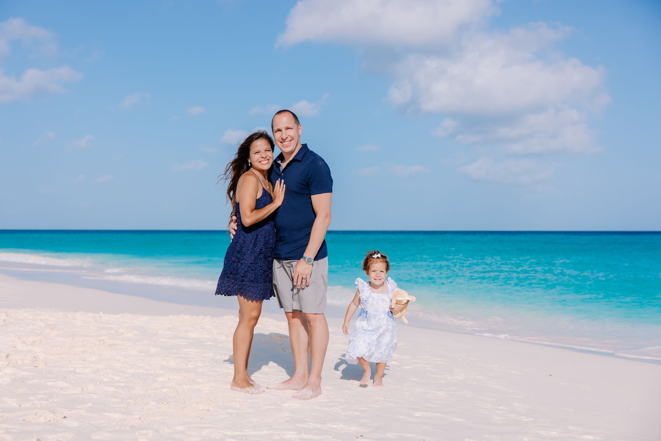 Family enjoying a beach day together on white sand with turquoise waters behind them.