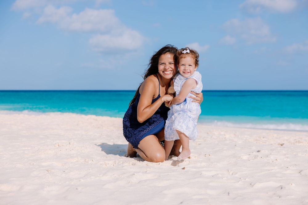 Family members sharing tender moments on a white sandy beach with turquoise ocean backdrop.