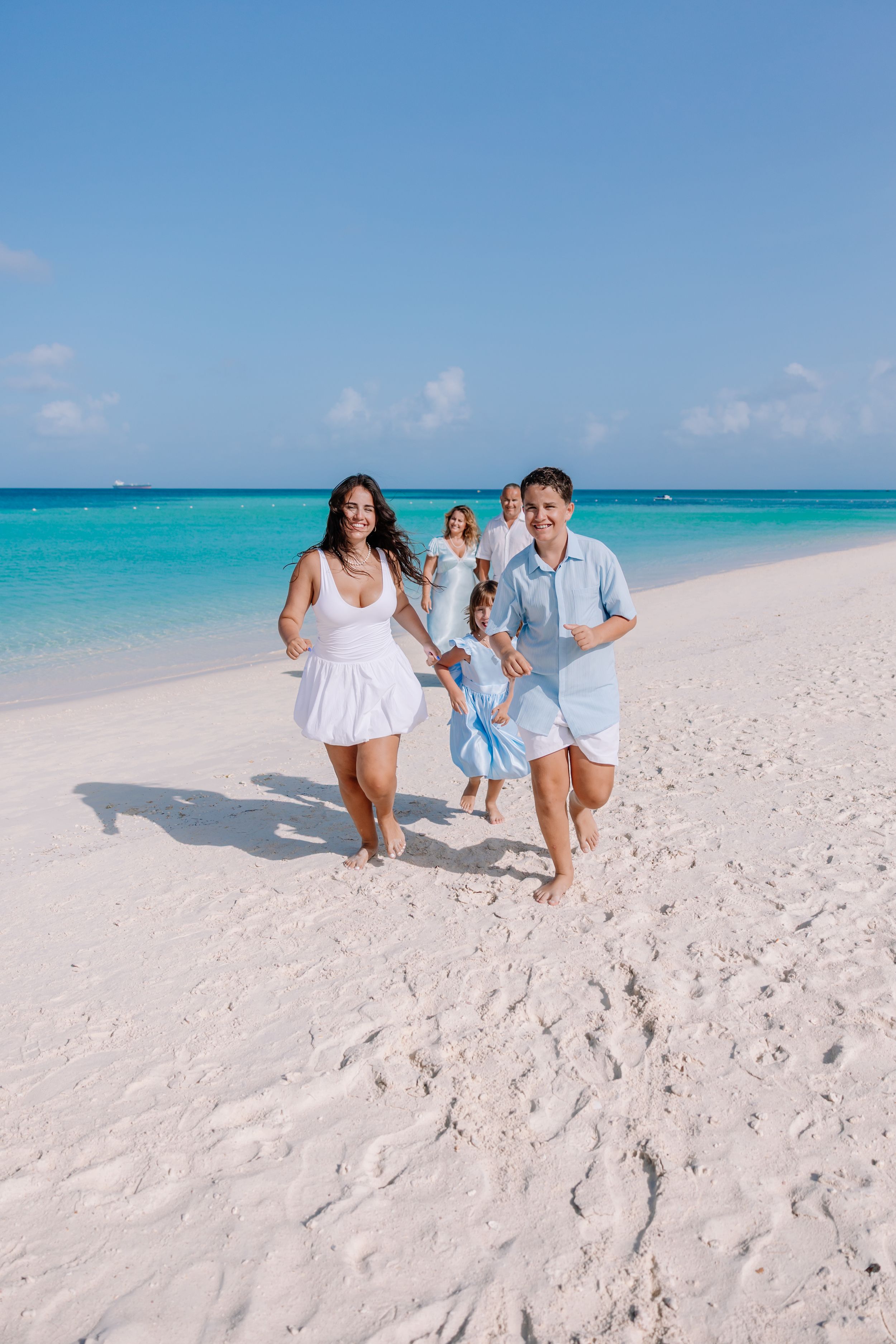 Family playing and walking together on pristine white sand beach with turquoise ocean backdrop.