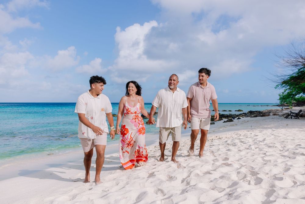 Family walking together on white sandy beach with turquoise ocean waters in the background.