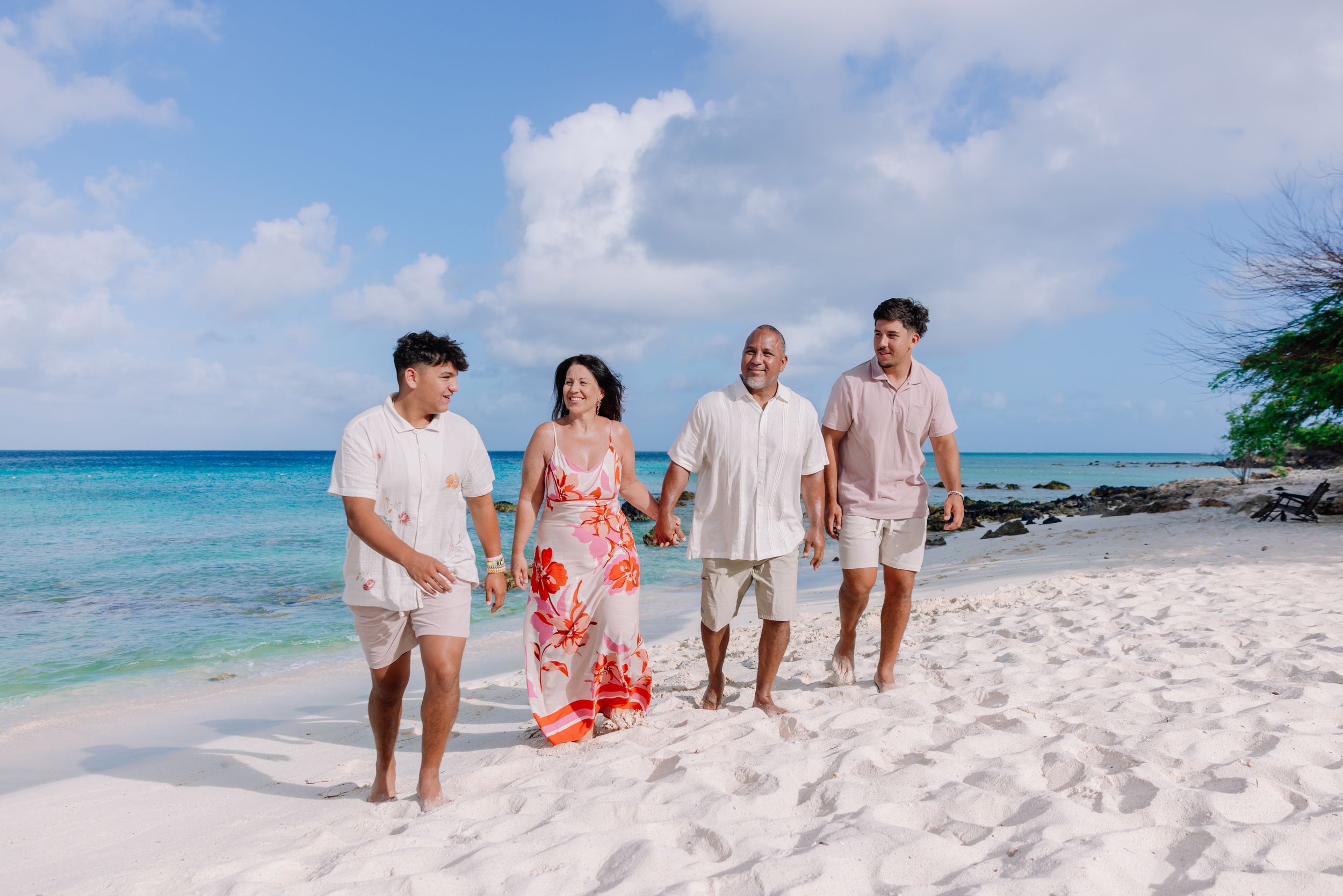 Family walking together on white sandy beach with turquoise ocean waters in the background.