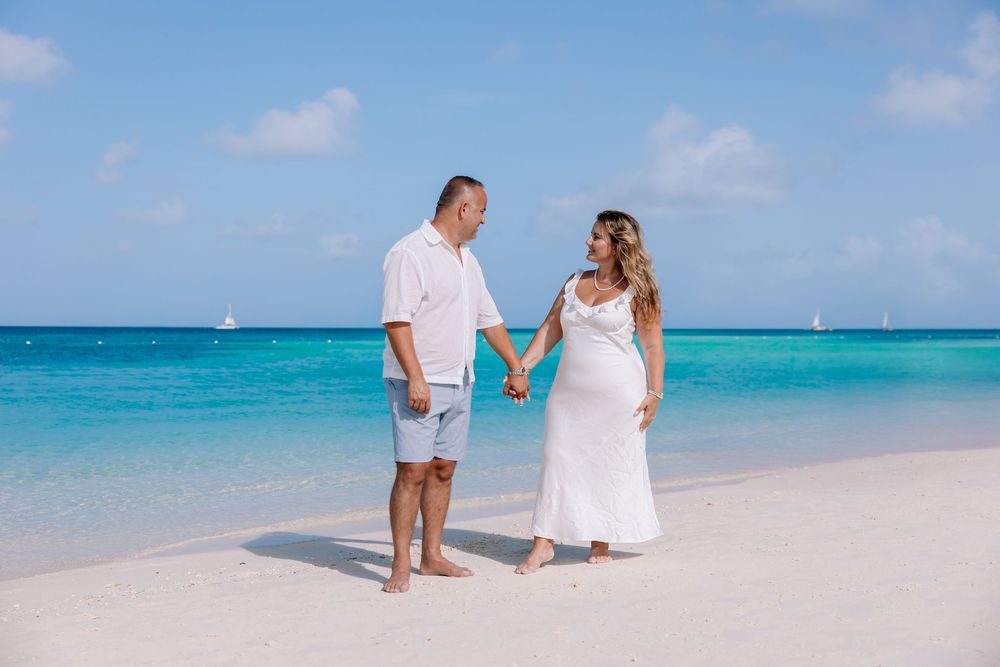 Family strolling along a pristine beach with sailboats visible on the turquoise horizon.