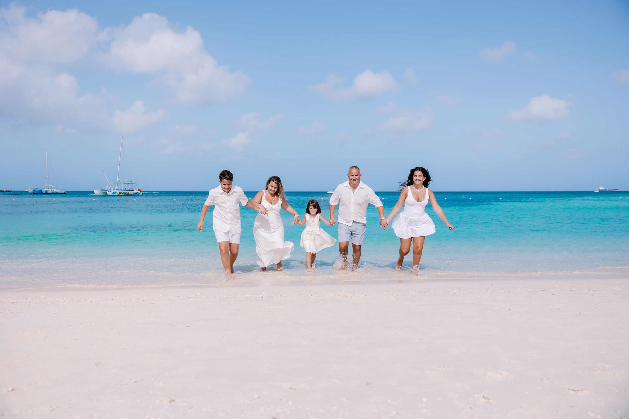 Family dressed in white walking along a beautiful Caribbean beach with crystal clear waters.