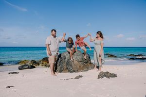 Family posing on rocky outcrops at a scenic beach with turquoise waters.