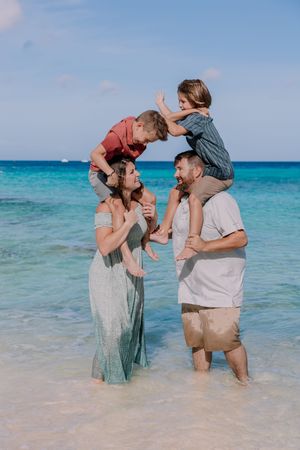Family members playing and lifting each other up while standing in crystal clear turquoise ocean waters.