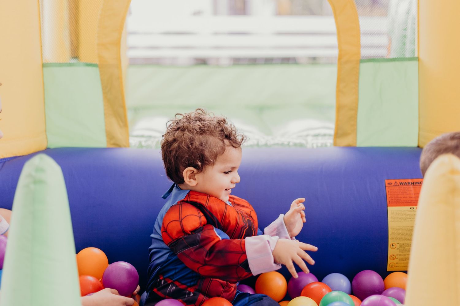 Young children play and interact with colorful toys and activities in a bright indoor playroom setting.