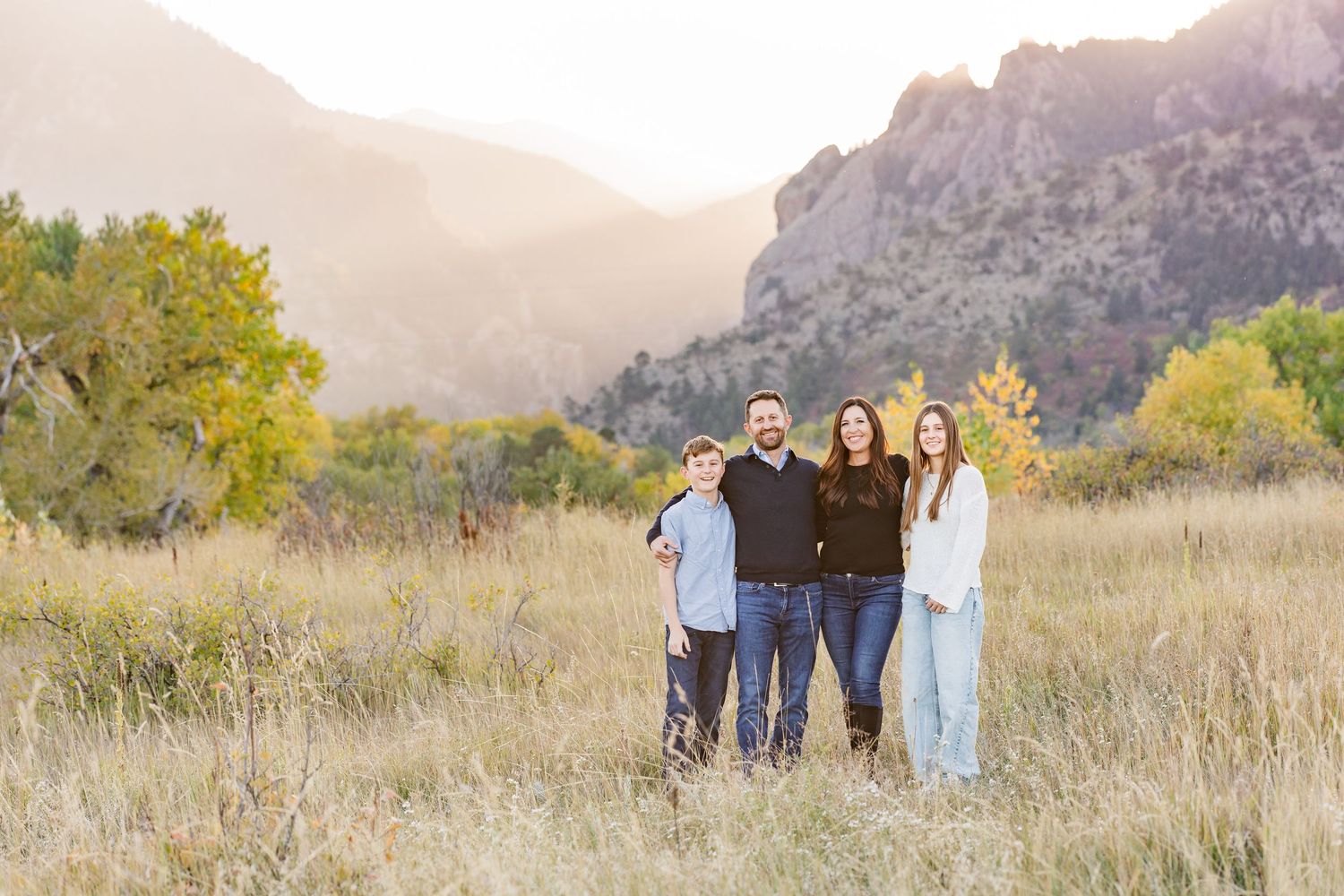A group of people walking together in a golden field with mountains and autumn foliage in the background at sunset.