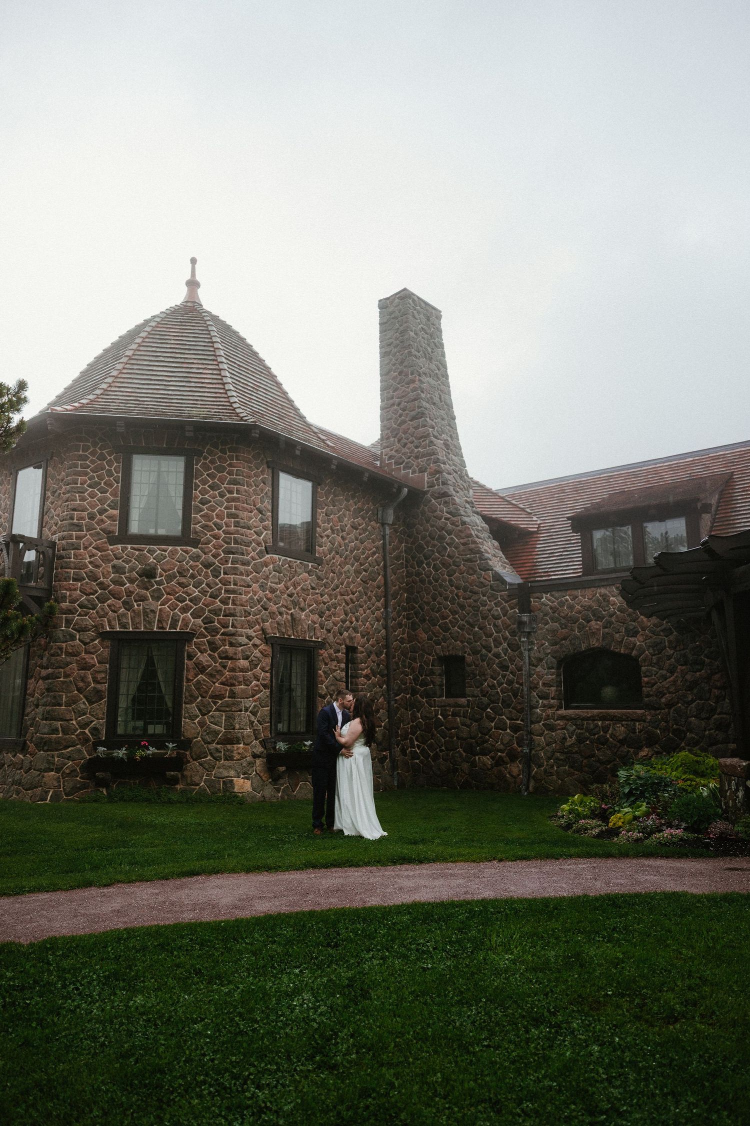A stone cottage with multiple chimneys and windows serves as backdrop for a wedding photoshoot.