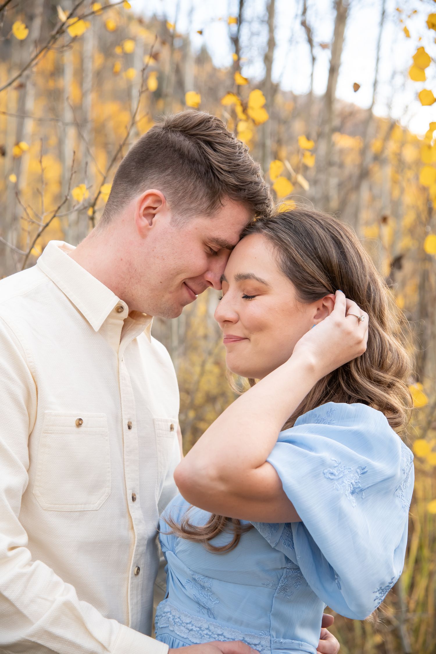 A couple embraces romantically in front of autumn birch trees with golden yellow leaves in the background during engagement photos in Vail
