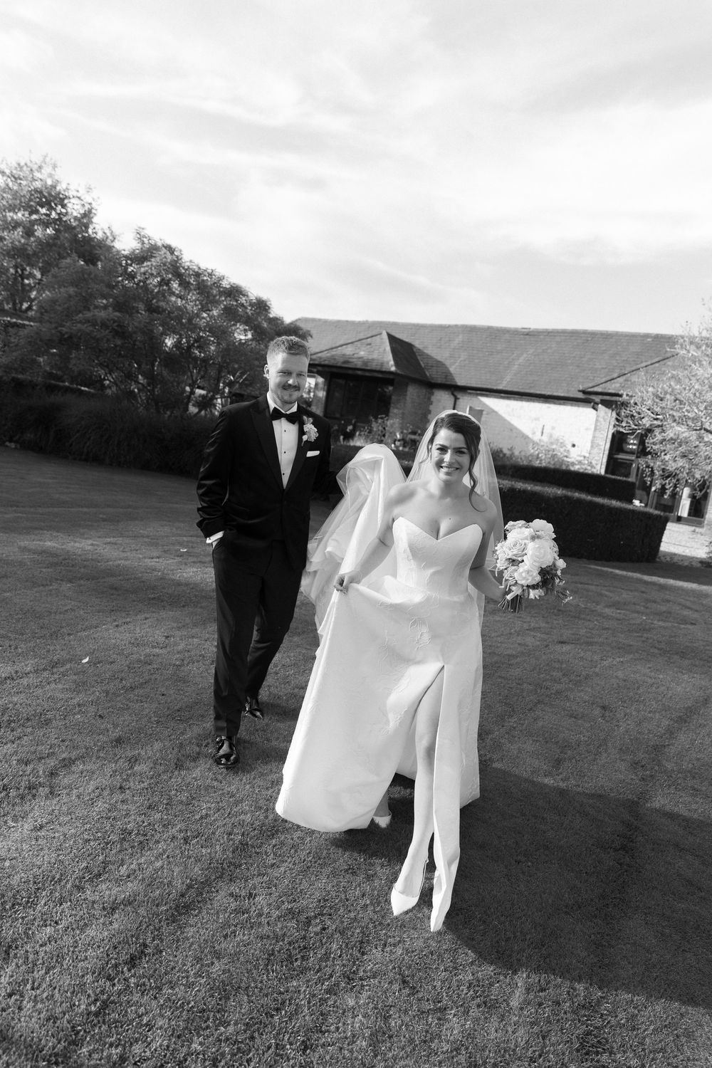Black and white photo of newlyweds walking across a grassy lawn.