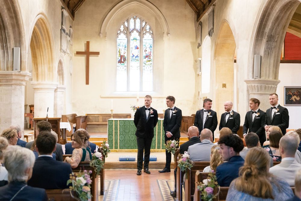 A church wedding ceremony with guests seated in wooden pews while viewing proceedings at the altar.