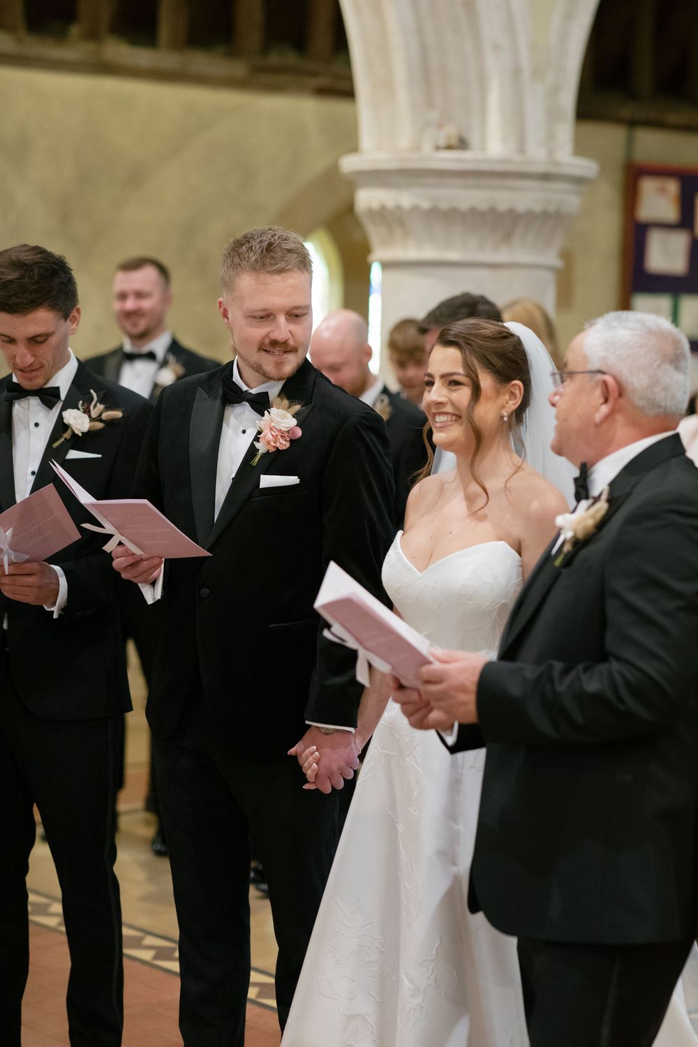 Wedding ceremony participants reading from programs inside a historic church with ornate columns.