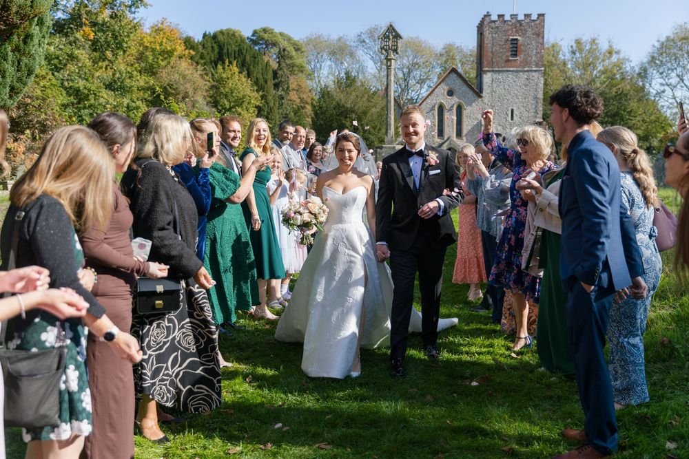 Wedding guests gather outdoors on a sunny autumn day near a historic building.