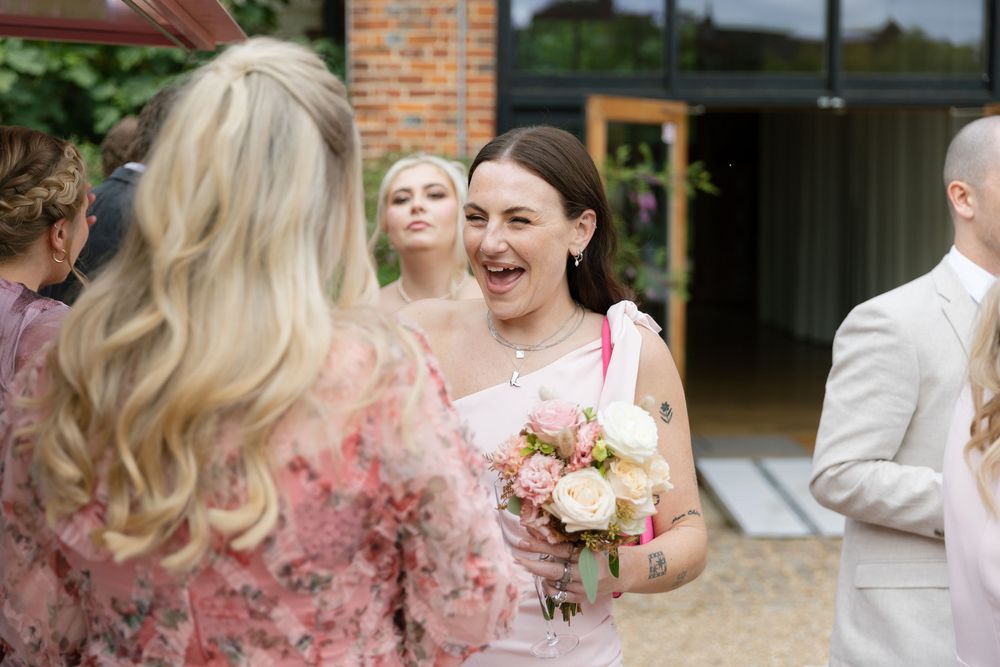 Wedding party in pink dresses and black tuxedos gathered outdoors for photos.