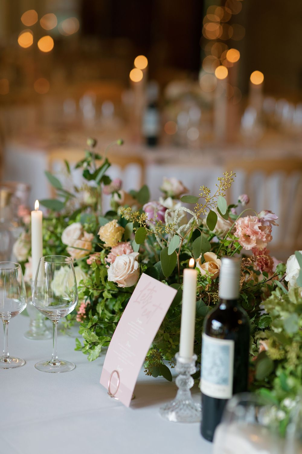 Wedding reception table decorated with lush greenery, white flowers and candlelight.