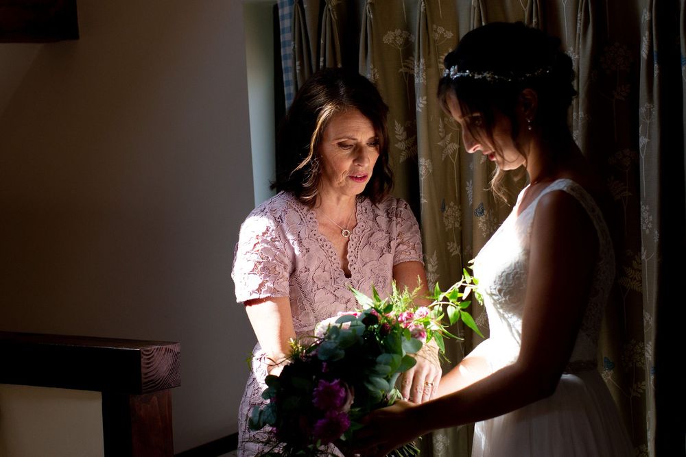 Bride holding bouquet in soft window light during intimate wedding preparations