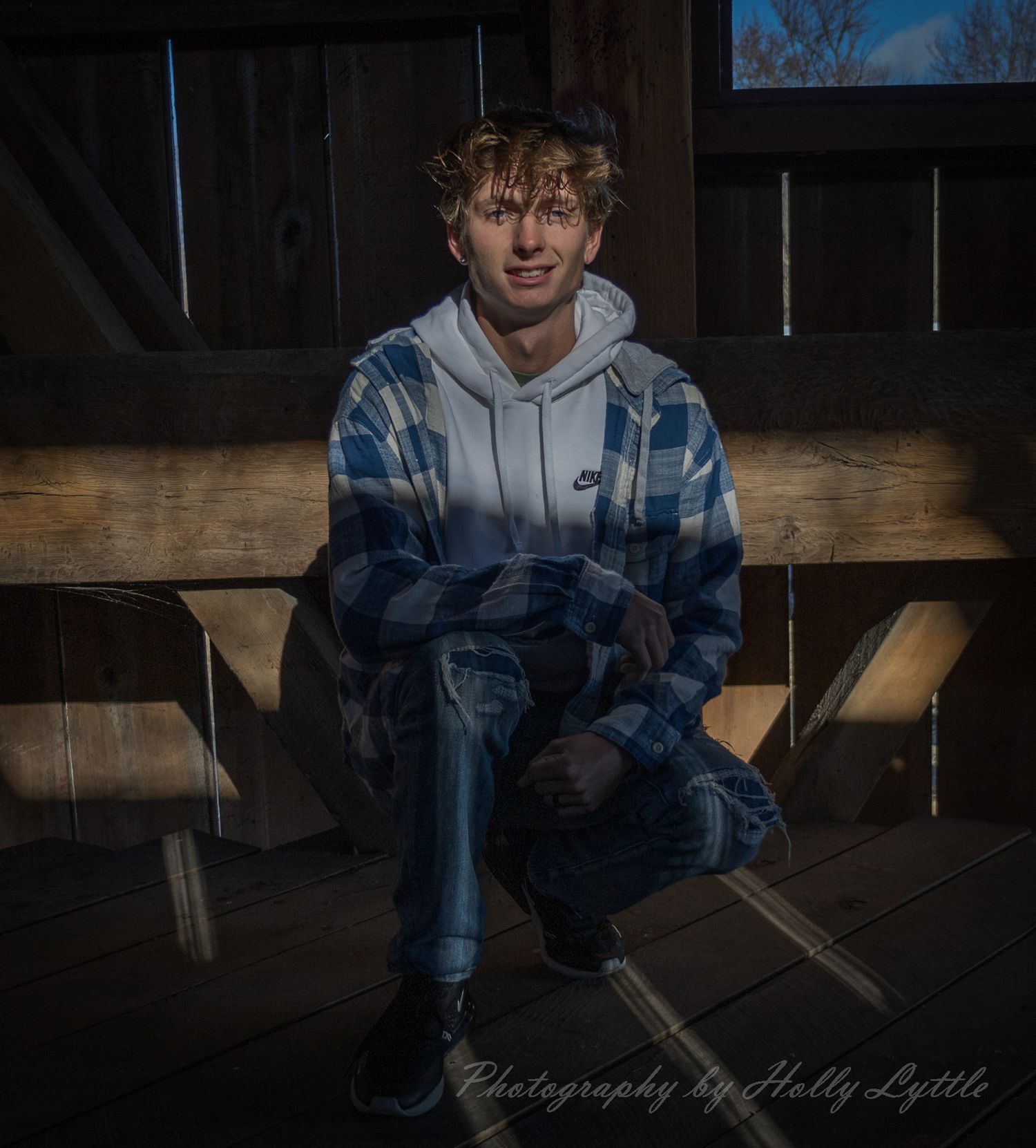 Person sits on wooden bench in rustic barn setting with dramatic lighting and moody atmosphere.
