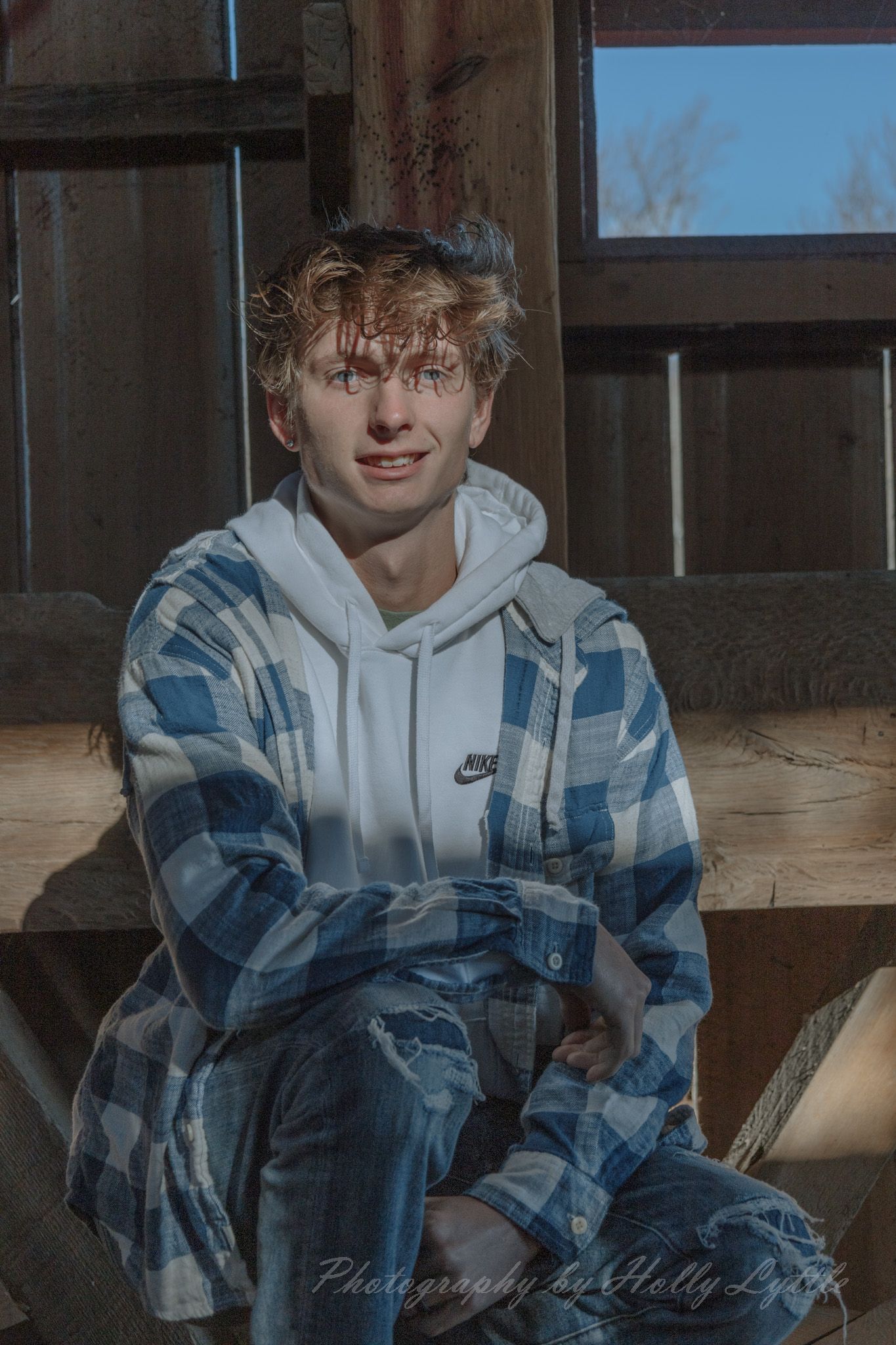 A person in a blue and white plaid Nike hoodie sits indoors in a casual pose.