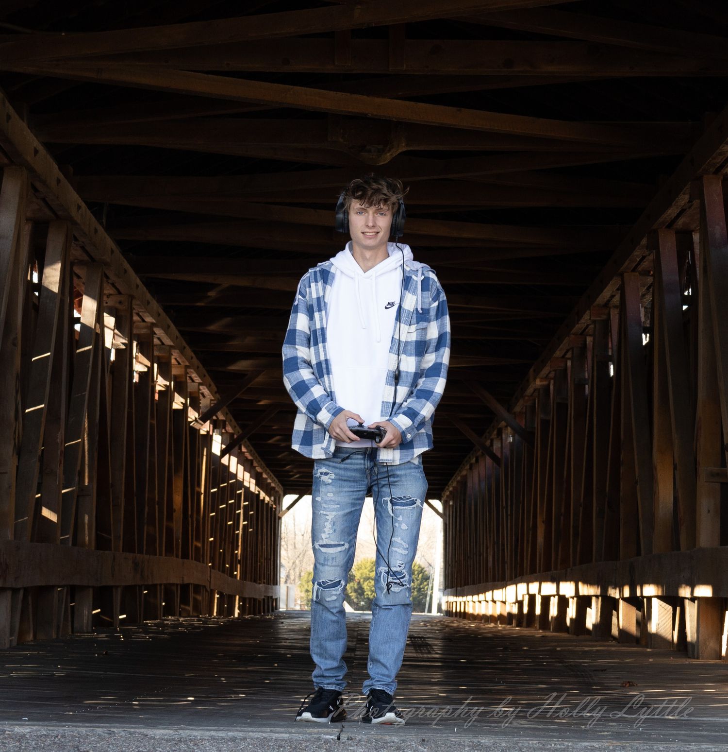 Person stands in middle of covered wooden bridge wearing plaid shirt and distressed jeans.